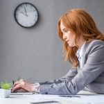 рыжеволосая бизнесвумен сидит за компьютером и выбирает Windows VPS для форекс